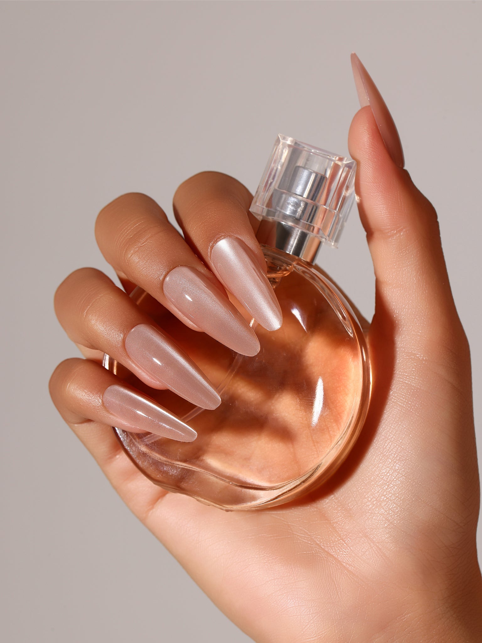 Hand wearing Pale Petal long stiletto nude blush pearl press-on nails luminous chrome look