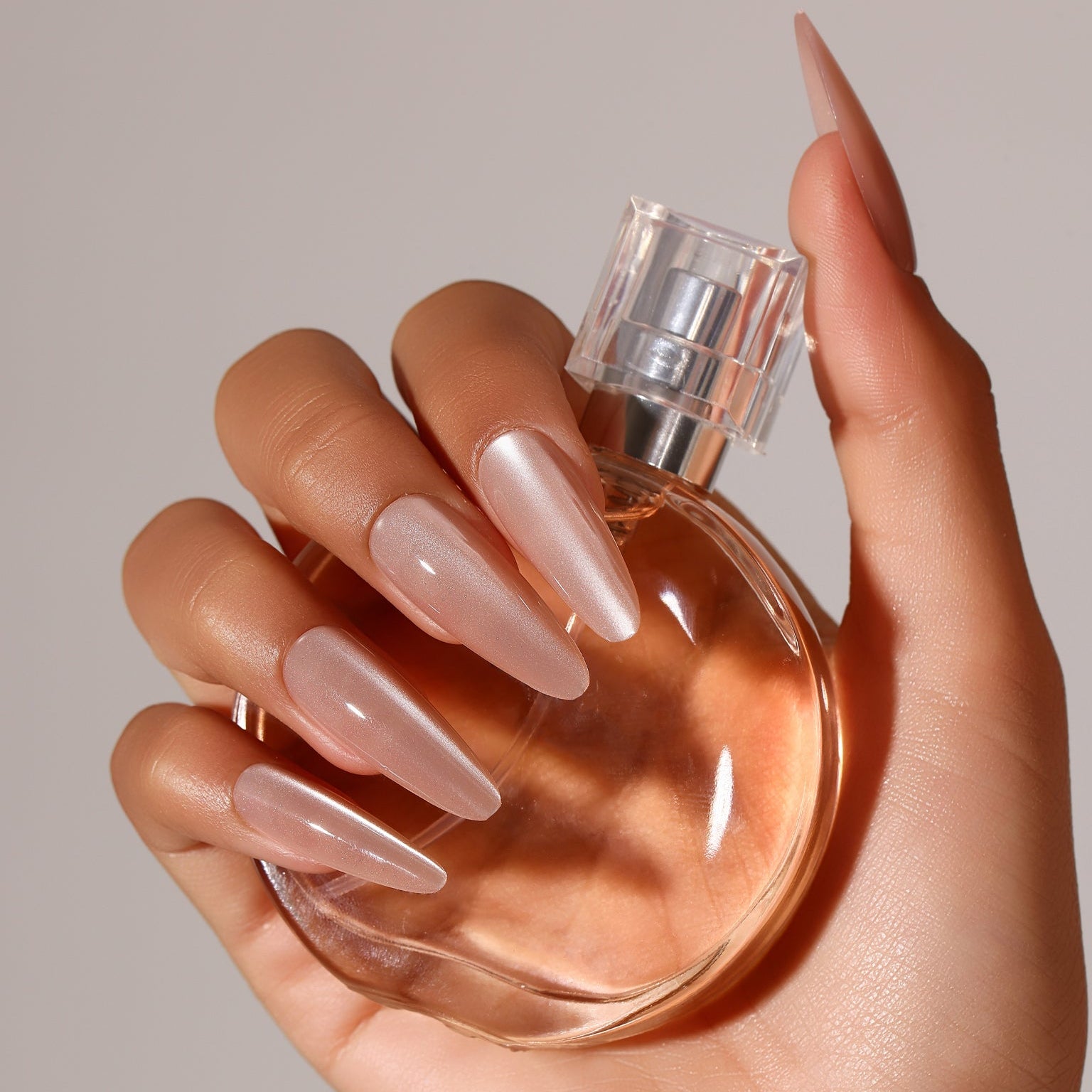 Hand wearing Pale Petal long stiletto nude blush pearl press-on nails luminous chrome look