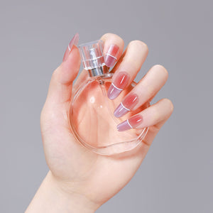 Hand holding perfume bottle wearing Violet Sugar long oval nude to violet ombre French press-on nails