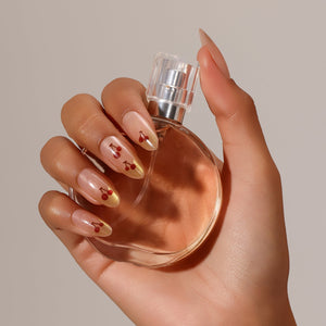 Hand wearing Cherry Spark Nails nude press-on nails with shimmering gold tips and tiny cherry nail art