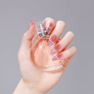 Hand holding a perfume bottle wearing purple ombré French oval press-on nails