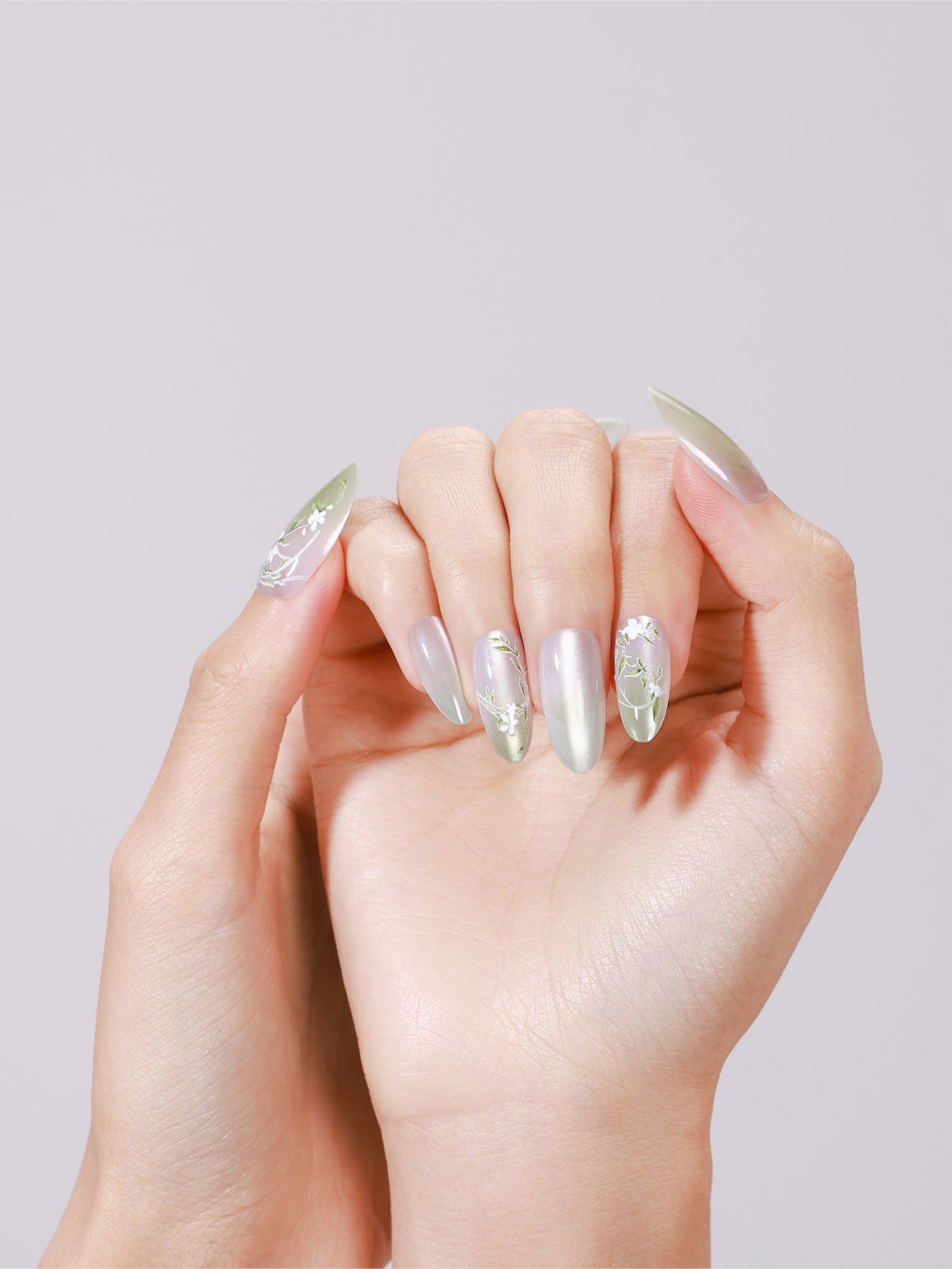 Hand wearing Spring Garden long almond mint green chrome press-on nails with white floral accent