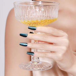 Hand holding champagne glass wearing Midnight Kiss long coffin midnight blue press-on nails