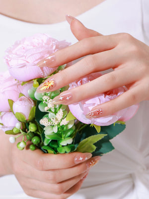 Close up of nude almond press on nails with gold firework bursts and white stars
