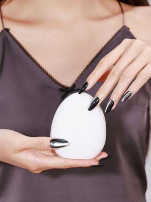 Hand wearing Noir Eclipse long almond glossy black chrome press-on nails reflective metallic shine