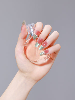 Hand holding a perfume bottle wearing green and gold French oval press-on nails