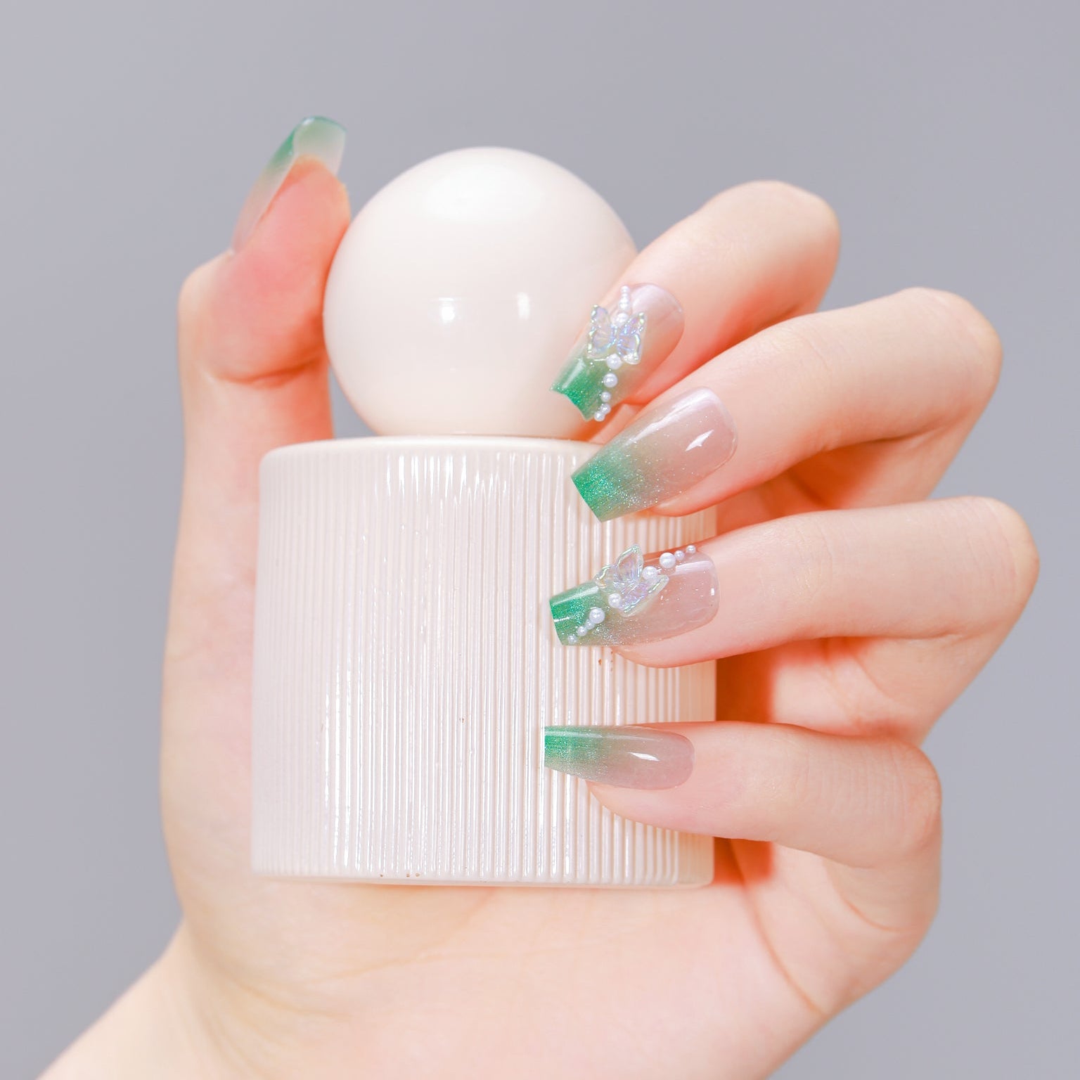 Hand holding perfume bottle wearing Garden Grace long coffin green French tip nails with 3D butterflies