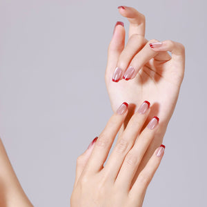 Close-up of both hands wearing nude and red French tip press-on nails in short square shape