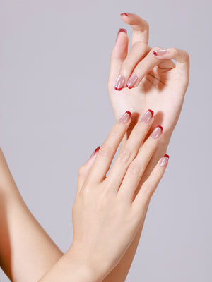 Close-up of both hands wearing nude and red French tip press-on nails in short square shape