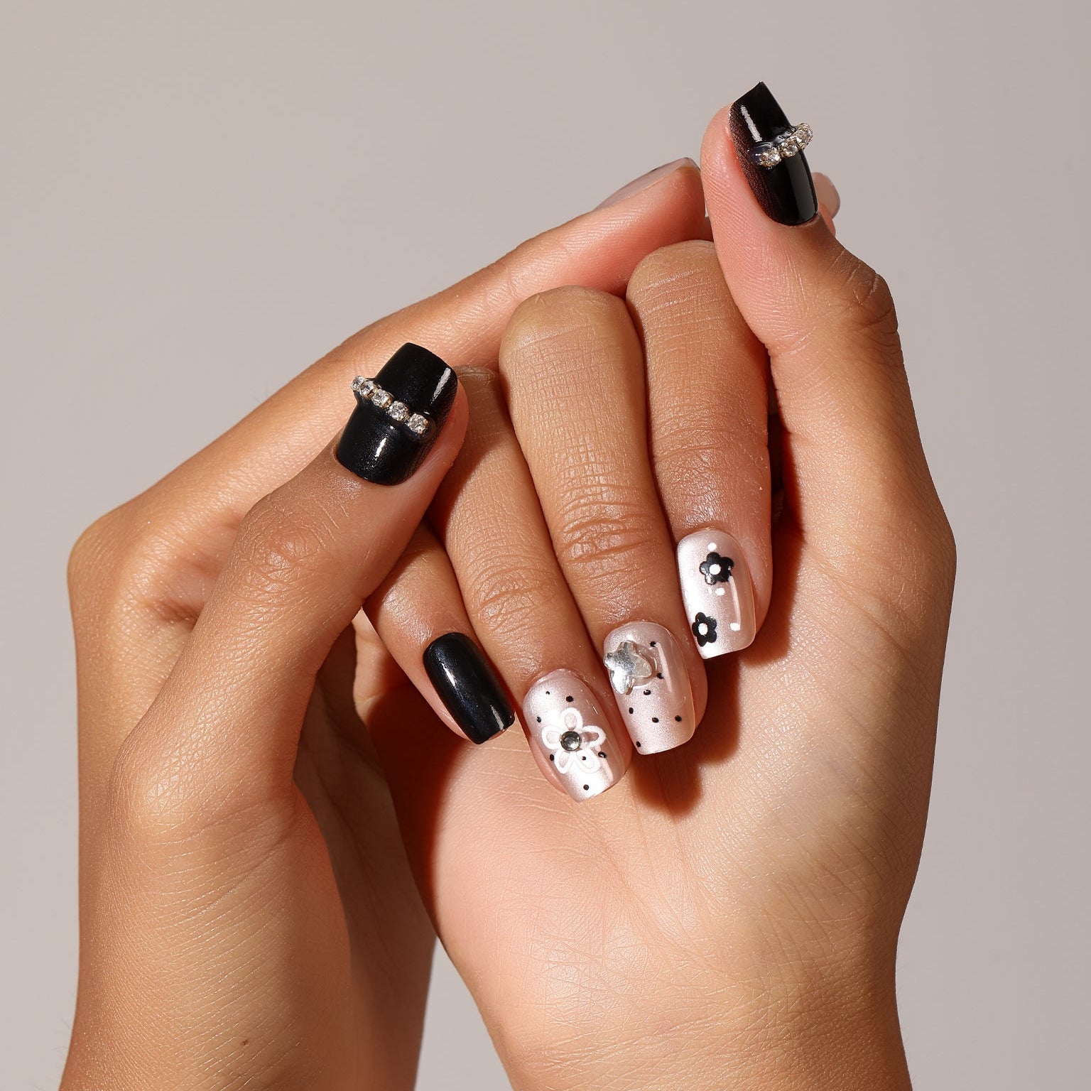 Hand wearing Gloss Bloom glossy nude press-on nails with black flower nail art and micro dot design