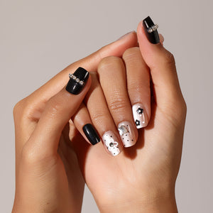 Hand wearing Gloss Bloom glossy nude press-on nails with black flower nail art and micro dot design