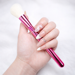 Almond press-on nails with nude base and white French tips, swirl accent nail and rhinestone cuticle detail, holding a pink metallic makeup brush on white studio background