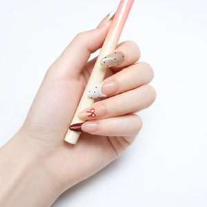 Almond shape press on nails with nude ombre base, red bow French tips and glossy salon finish, hand holding pen