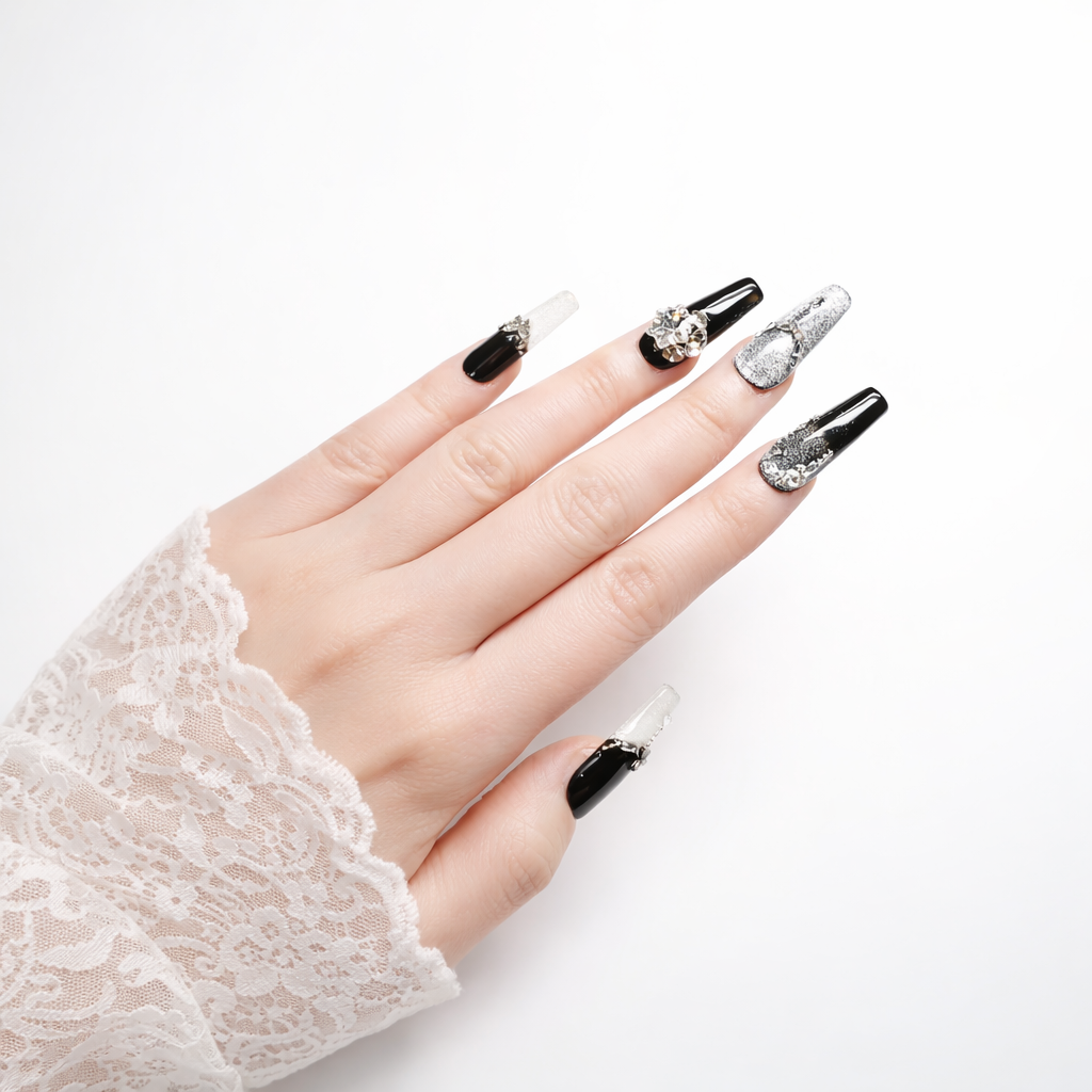 Hand model wearing black and silver coffin press on nails with glitter ombre, rhinestone accents and 3D crystal charm on white background