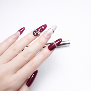Side angle view of burgundy almond press on nails with French design, nude ombre base, and crystal rhinestone details