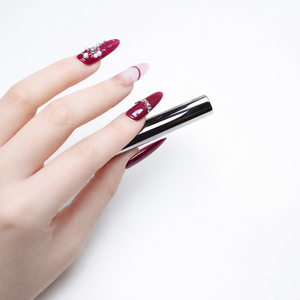 Burgundy Almond French press on nails with nude ombre base and crystal rhinestones shown on hand holding a sleek metal tool