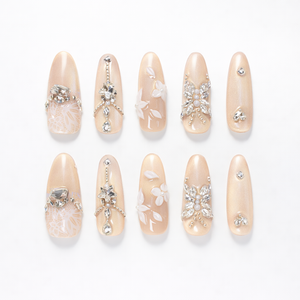 Champagne nude almond press on nails set with crystal rhinestones, 3D floral accents and glossy finish shown as a 10 piece handmade set
