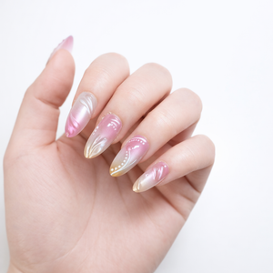Close-up angled view of almond-shaped pink and gold ombre press-on nails with pearl detailing on elegant white skin model hand in professional studio lighting.