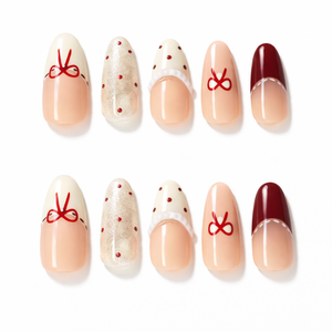 Set of almond press on nails featuring nude ombre base, red bow French tips, polka dot accents and glossy gel finish