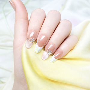 Spring nude French press on nails with white floral tips, shimmer accent nail and silver butterfly charm on a soft yellow satin background