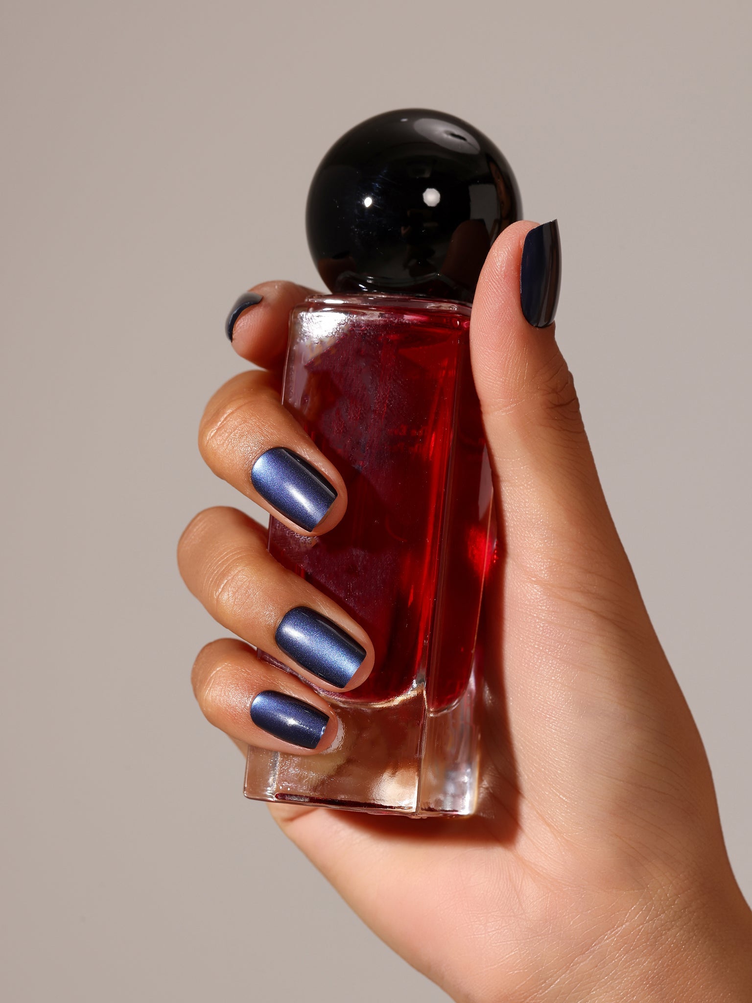 Hand holding red perfume bottle with metallic navy blue press on nails