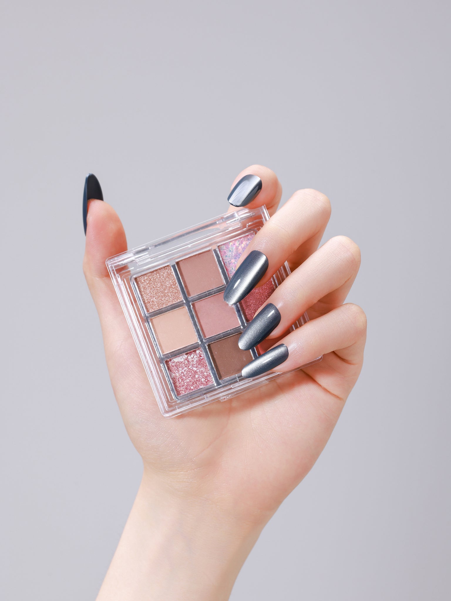 Hand wearing Smoky Quartz long oval smoky gray cat eye press-on nails holding makeup palette