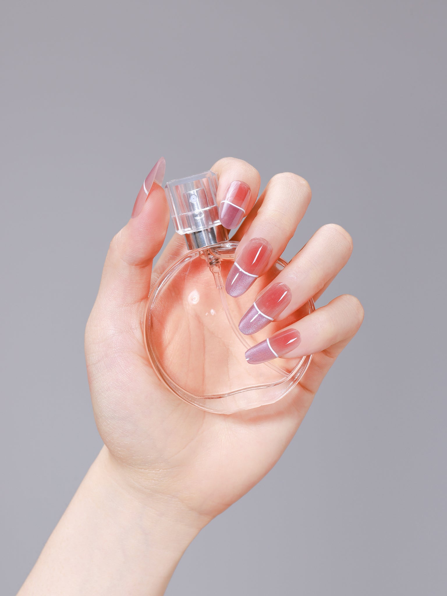 Hand holding a perfume bottle wearing purple ombré French oval press-on nails