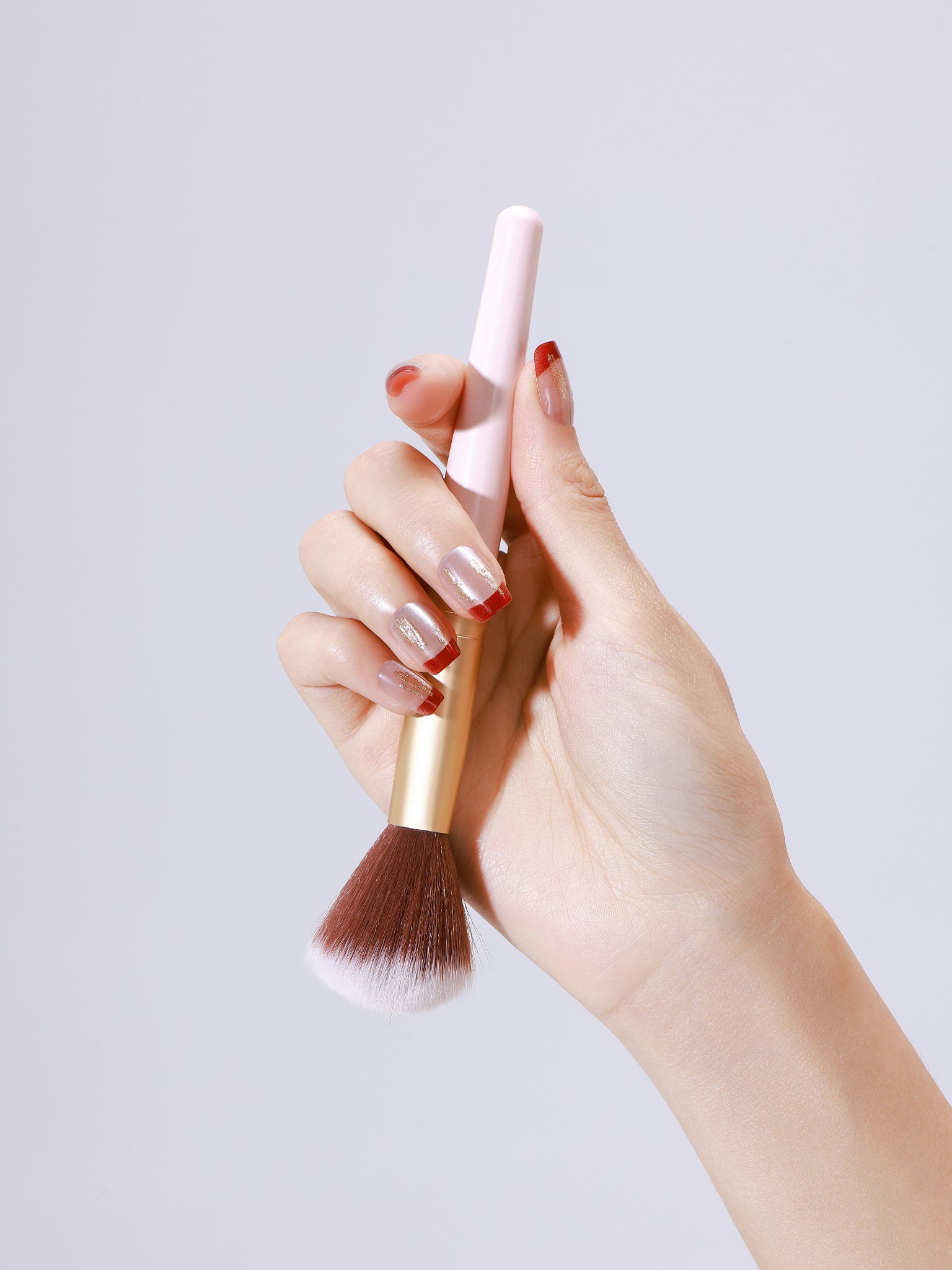 Close up of Fortune Spark nude press on nails with red French tips and gold foil accents