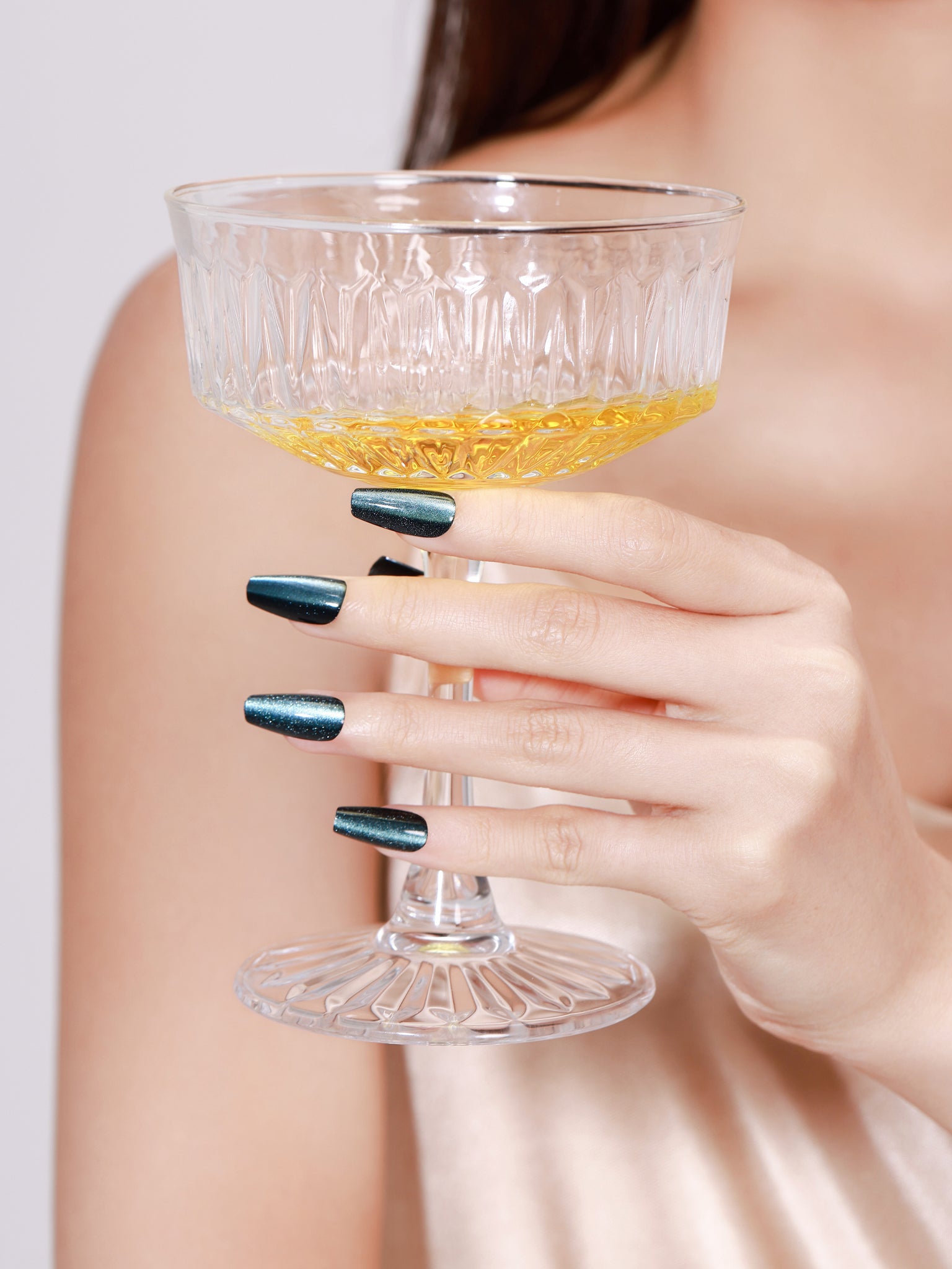 Hand holding champagne glass wearing Midnight Kiss long coffin midnight blue press-on nails