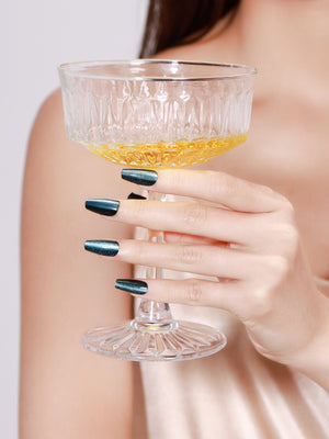Hand holding champagne glass wearing Midnight Kiss long coffin midnight blue press-on nails