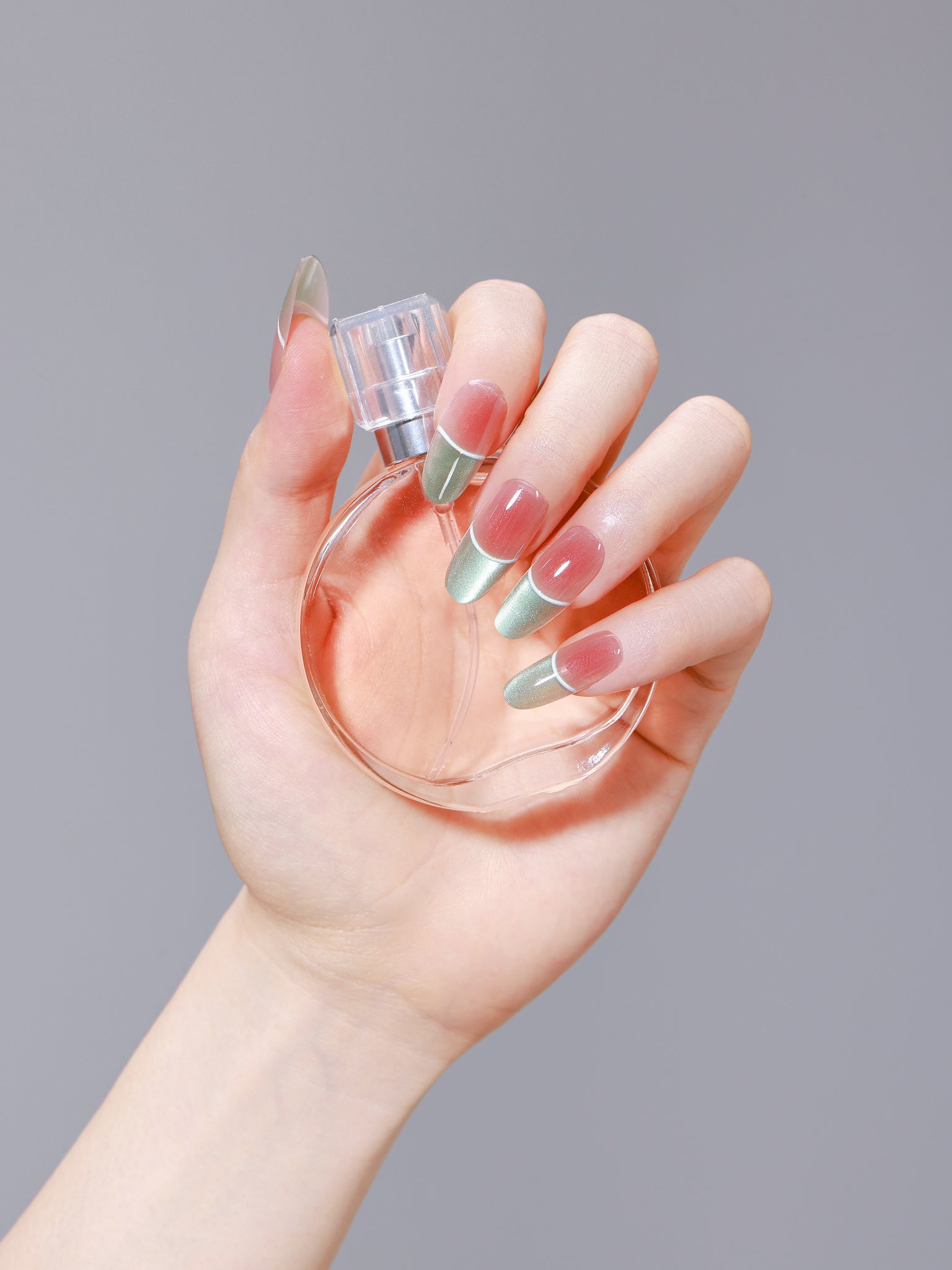 Hand holding a perfume bottle wearing green and gold French oval press-on nails