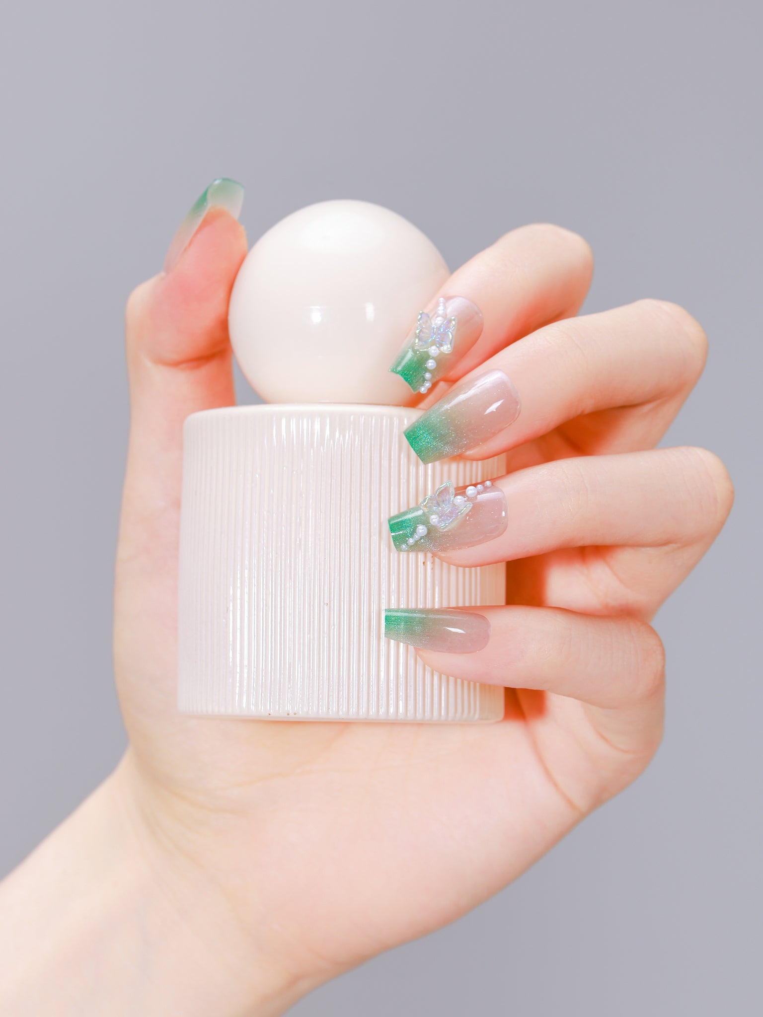Hand holding perfume bottle wearing Garden Grace long coffin green French tip nails with 3D butterflies