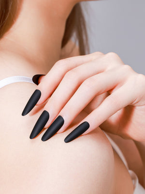 Hand wearing Noir Nights long oval matte black press-on nails with velvety gel finish