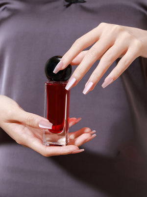 Hand holding perfume bottle with Peach Kiss long coffin peach nude press-on nails