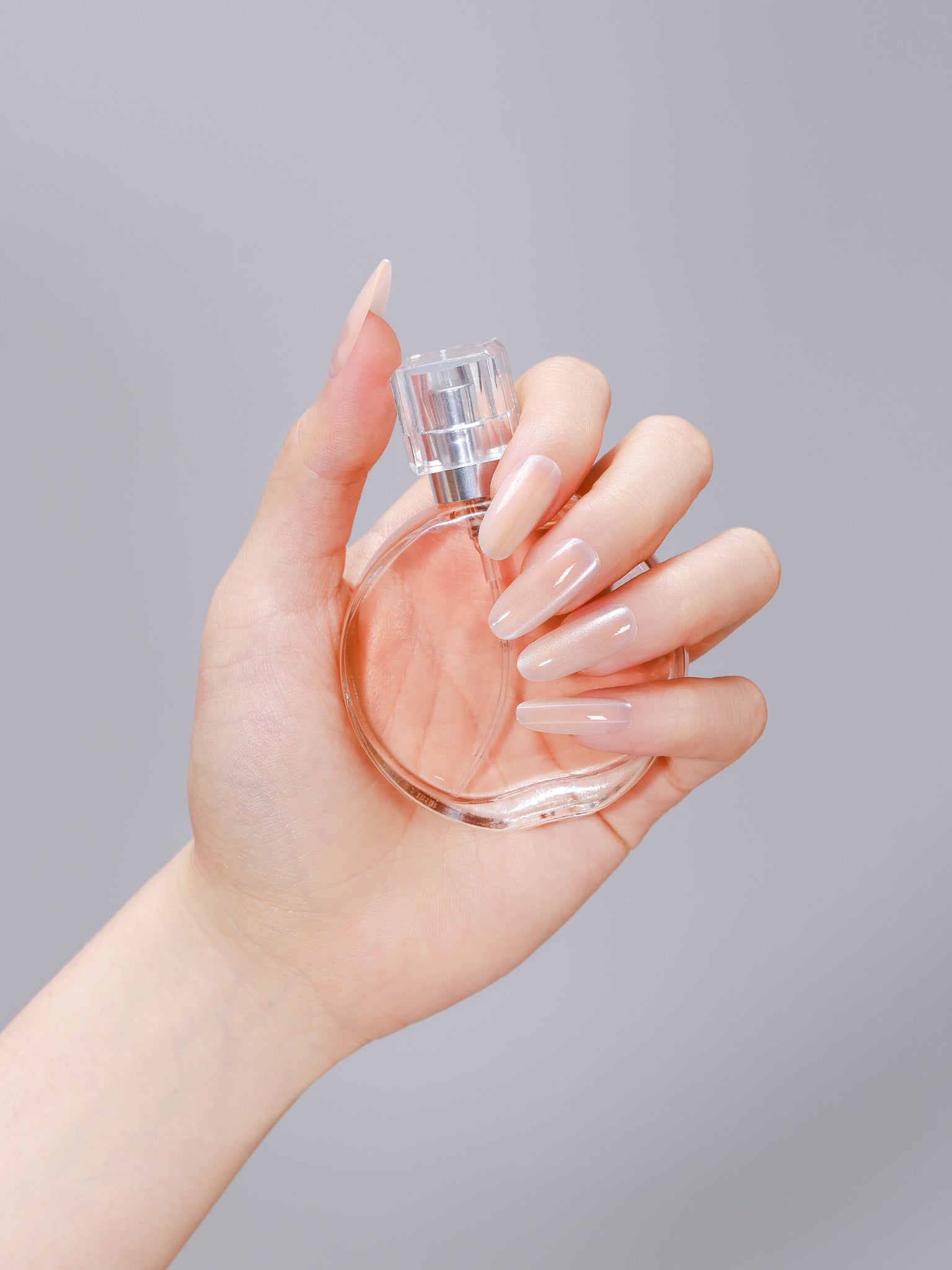 Hand wearing beige long oval peach nude press-on nails made from PMMA acrylic