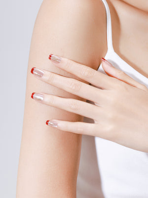 Close up of Fortune Spark nude press on nails with red French tips and gold foil accents