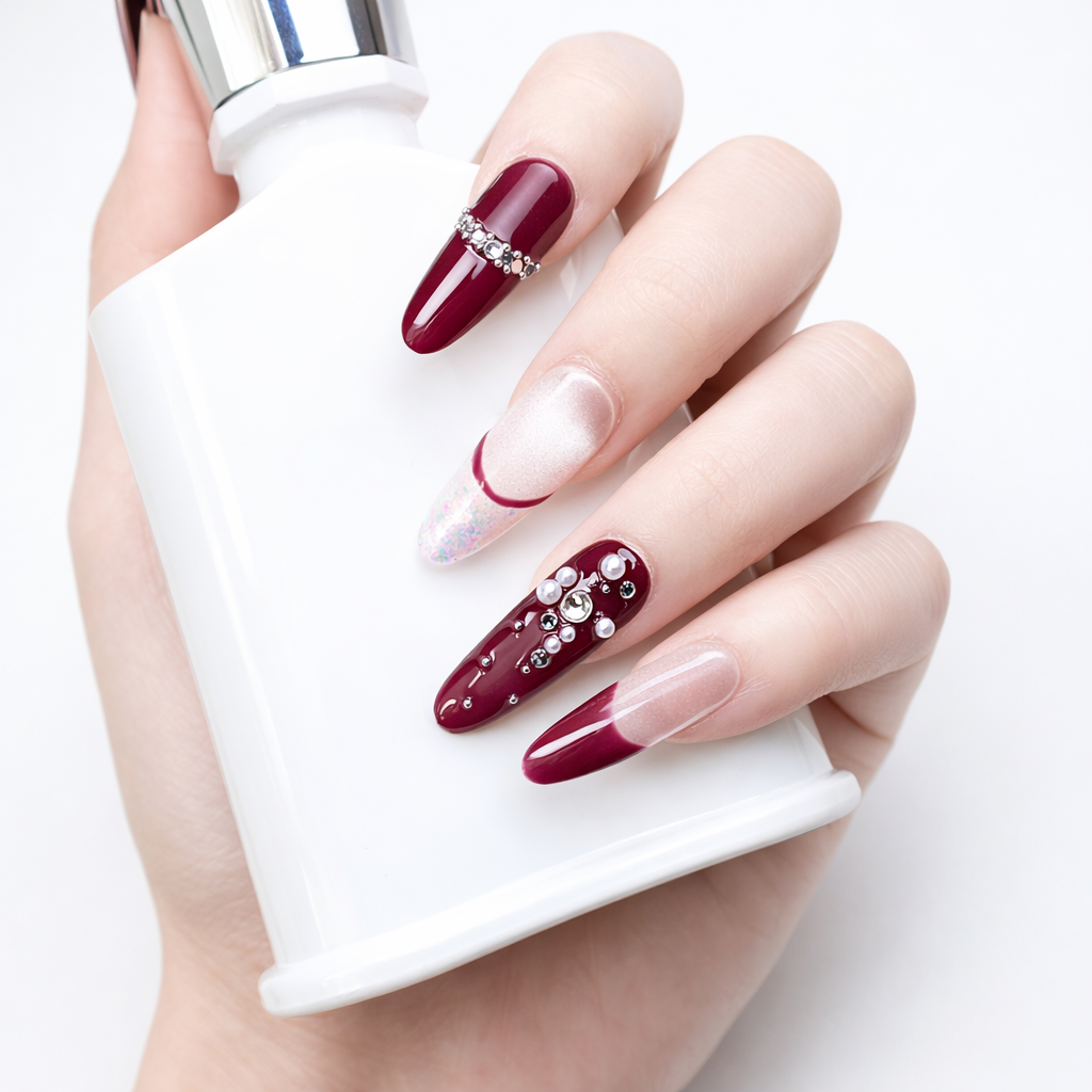 Hand model holding a white bottle while wearing burgundy French press on nails with nude ombre base and crystal rhinestone accents
