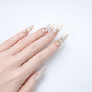 Luxury bridal style champagne nude almond press on nails with rhinestone embellishments and delicate floral nail art on a neutral glossy base
