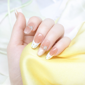 Spring nude French press on nails with white floral tips, shimmer accent nail and silver butterfly charm on a soft yellow satin background
