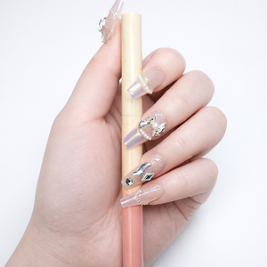 Coffin press on nails with sheer glitter base, pearl edge detailing, silver bow charms, and iridescent crystal embellishments shown holding object