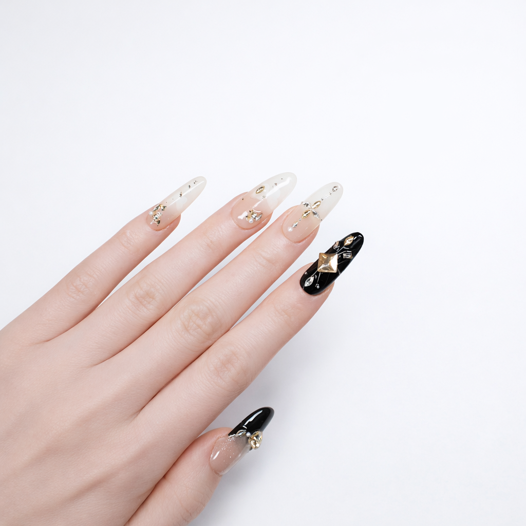 Elegant long almond press-on nails with sheer nude base, black statement nail, champagne crystal accent, gold foil details, and high-gloss salon-style finish on white background.