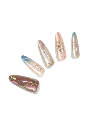 Close-up Celestial Drift stiletto press-on nails nude to blue ombre with gold foil tip and speckled finish